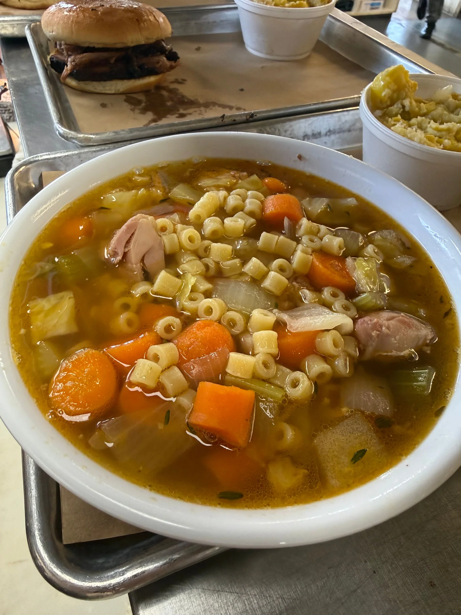 A bowl of soup with pasta, vegetables and pieces of meat