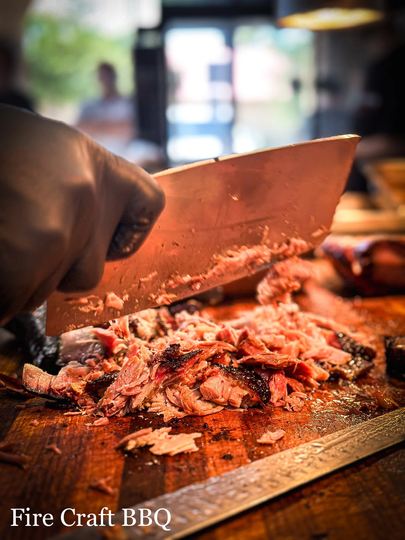 A cook chopping smoked meat with a cleaver on a wooden board
