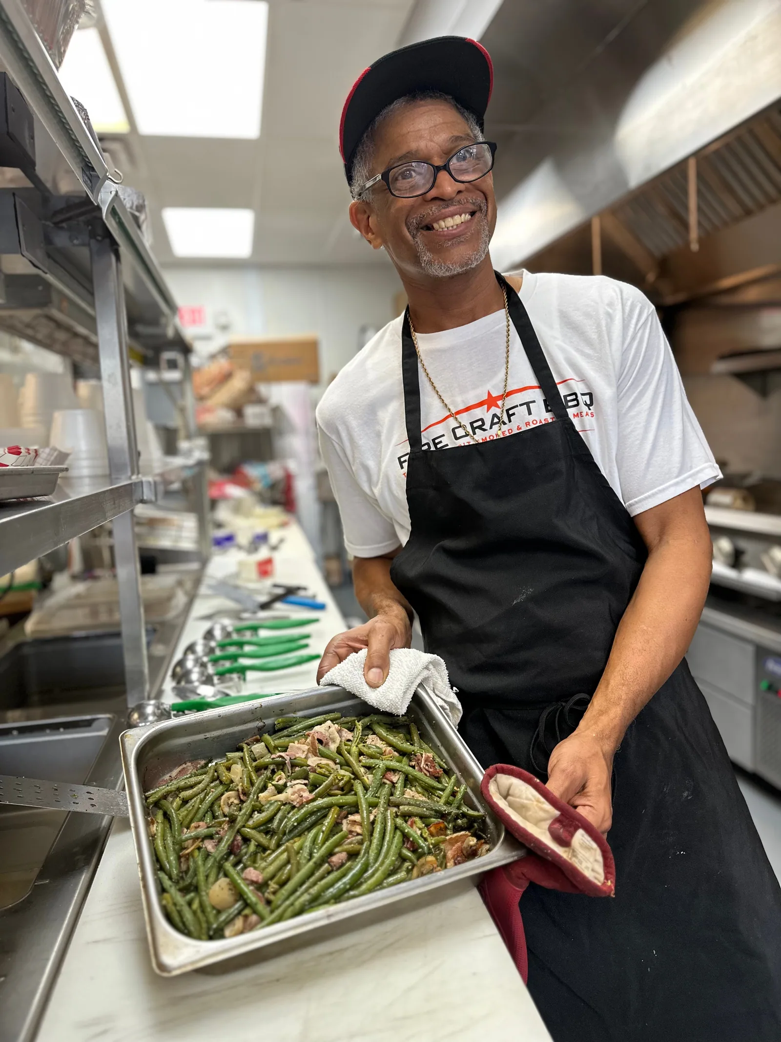 A smiling Fire Craft cook holding a tray of green beans