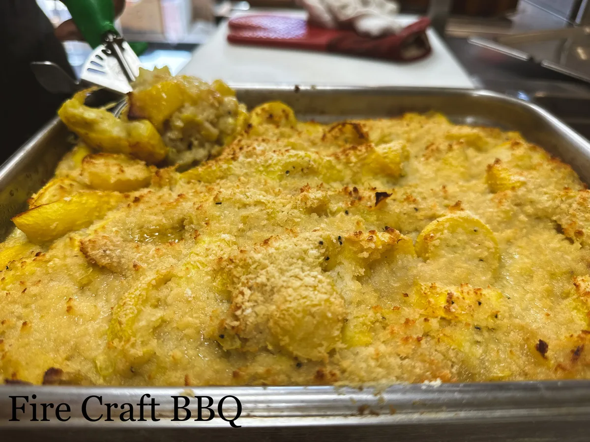 A tray of golden-topped squash casserole with a serving spoon
