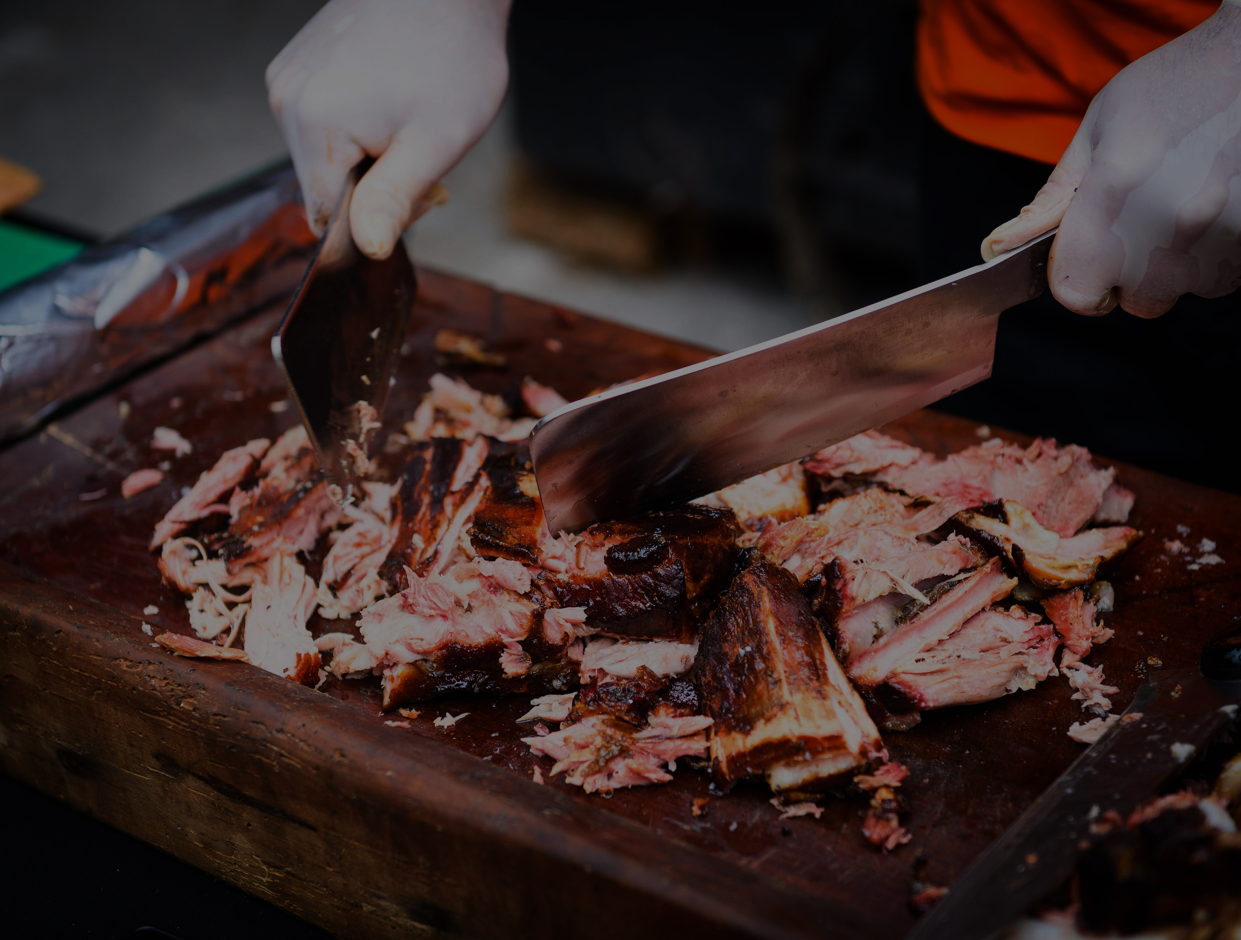 Chef Hands cutting Grilled spare beef or pork back ribs prepared in smoker with a hatchet. Delicious roasted cuts of meet made on barbecue smoker on a wooden cutting desk.